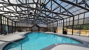 An indoor swimming pool with a glass ceiling, stone walls, and lounge chairs. - Dollywood 1.2 miles ►Easy Roads ►Indoor Resort Pool ►Hot Tub ►Game Room ►Dogs Ok (Sevierville)