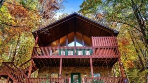 Une cabane à deux étages, avec une façade en pierre, un balcon à l’étage supérieur et un escalier menant à l’entrée.