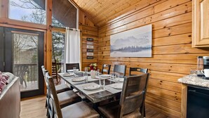 L'intérieur d'un chalet en bois, avec une table à manger dressée pour quatre personnes, une machine à café et un tableau représentant des montagnes accroché au mur.