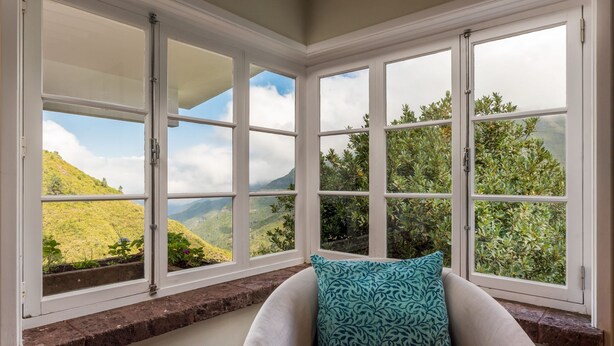 Ein Zimmer mit großen Fenstern und Blick auf grüne Hügel und einen bewölkten Himmel.