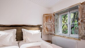 Ein Schlafzimmer mit einem hölzernen Kopfende, weißer Bettwäsche und einem Fenster mit Blick auf Bäume.