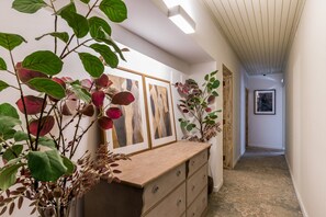 A hallway with a wooden dresser, framed artwork, and potted plants.