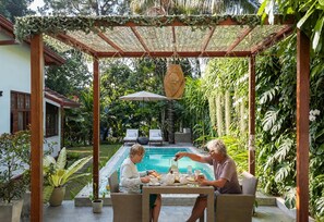 A covered outdoor seating area with a pool and lush greenery in the background. - Colonial Residence Kandy  (Kandy)