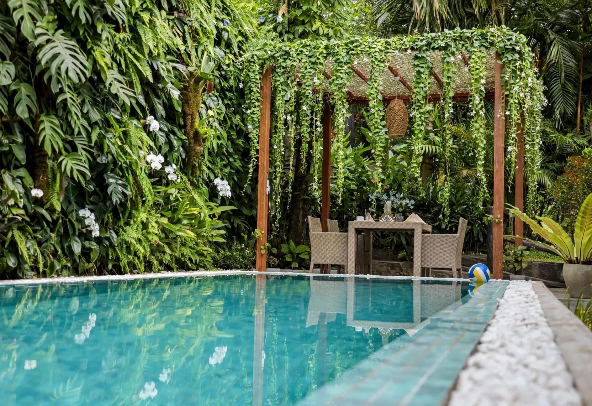 A swimming pool with a wooden pergola and wicker furniture.