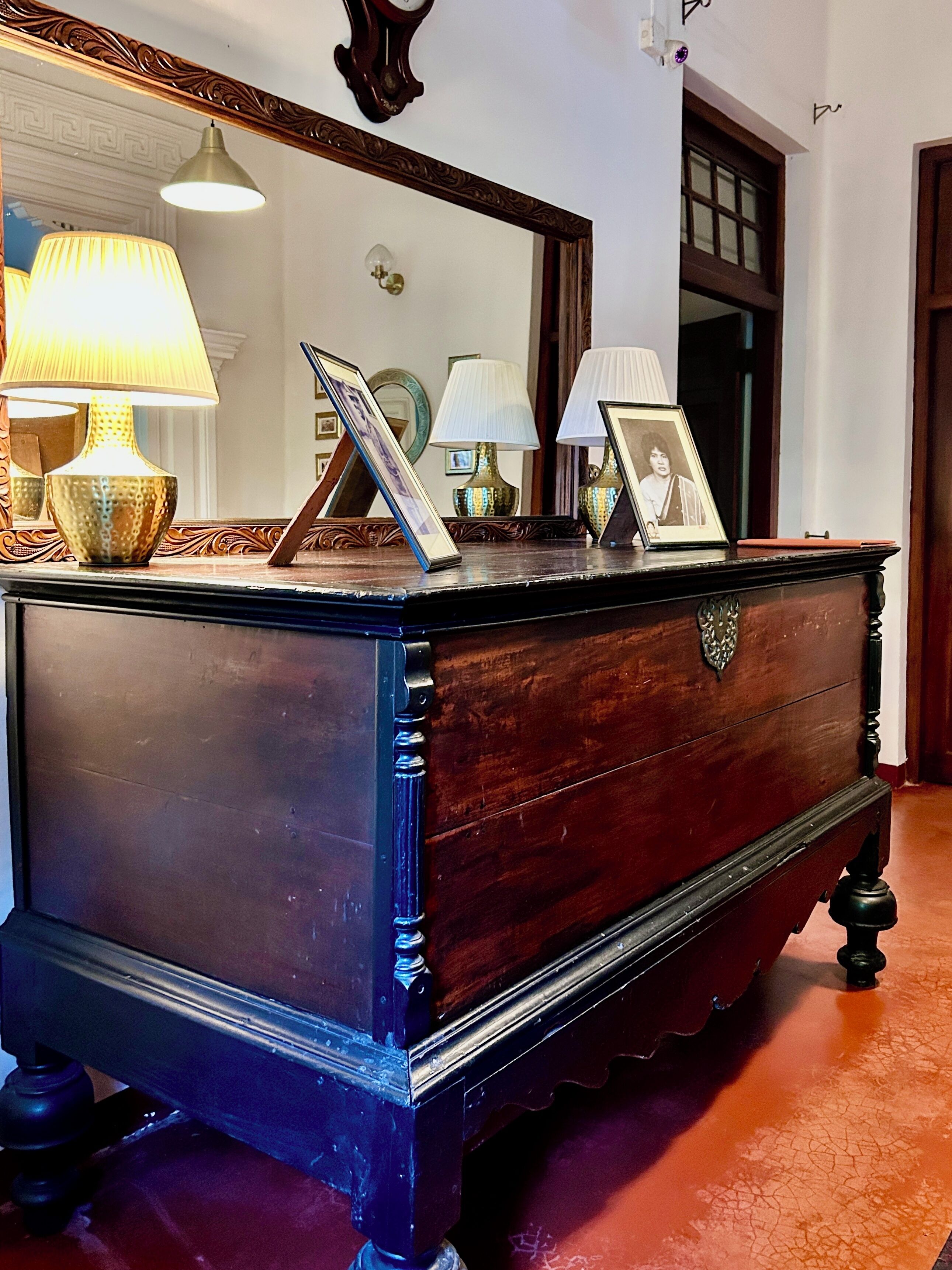 A dark wooden dresser with ornate carvings, a mirror above it, and three lamps on the dresser.