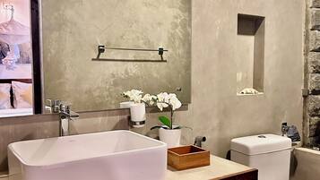 A modern bathroom with a large white sink, a wooden vanity, a toilet, and a mirror above the sink.