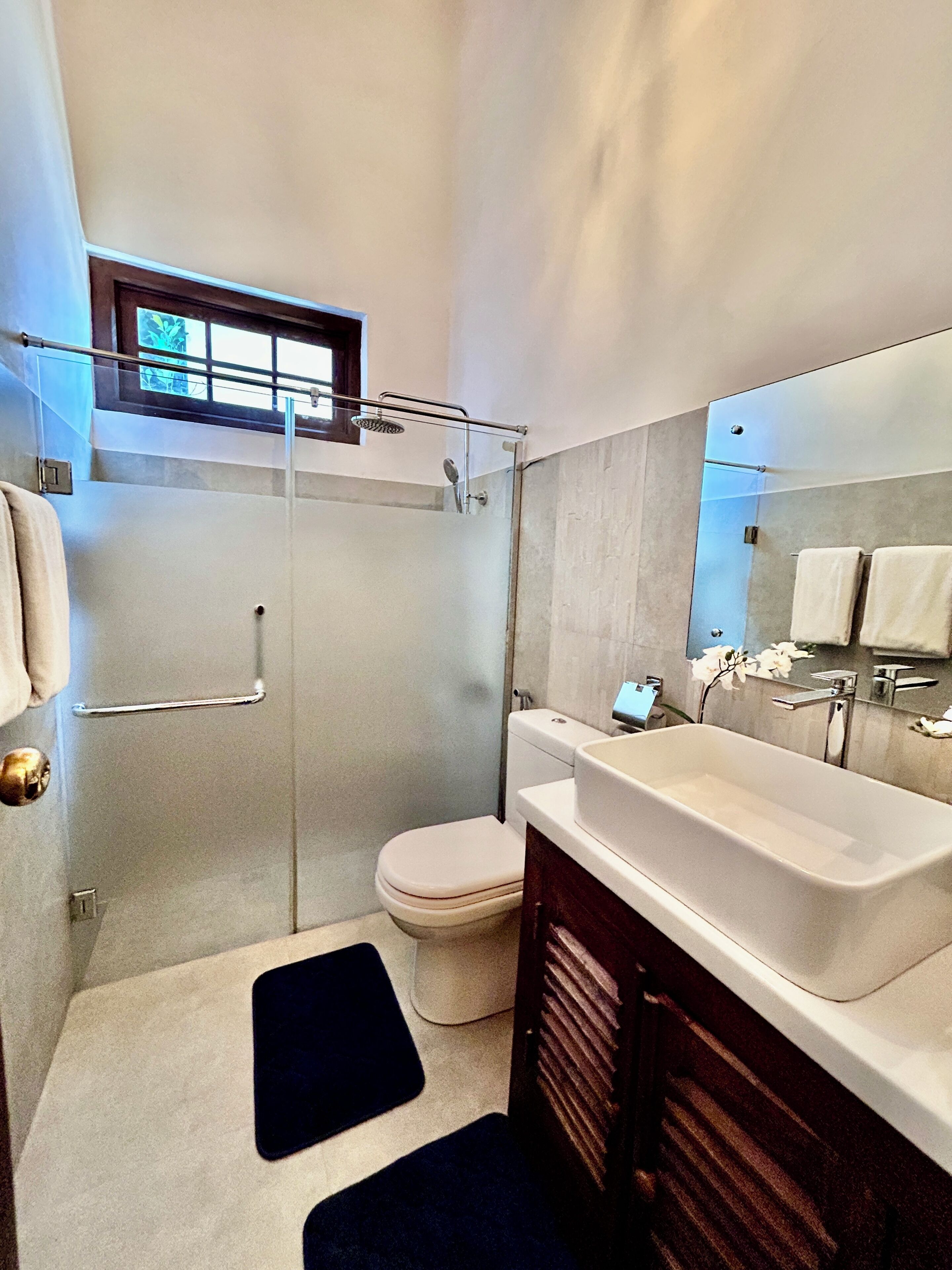 Et moderne badeværelse med et glasafskærmet brusebad, et hvidt toilet, et stort badekar og en vask med spejl.