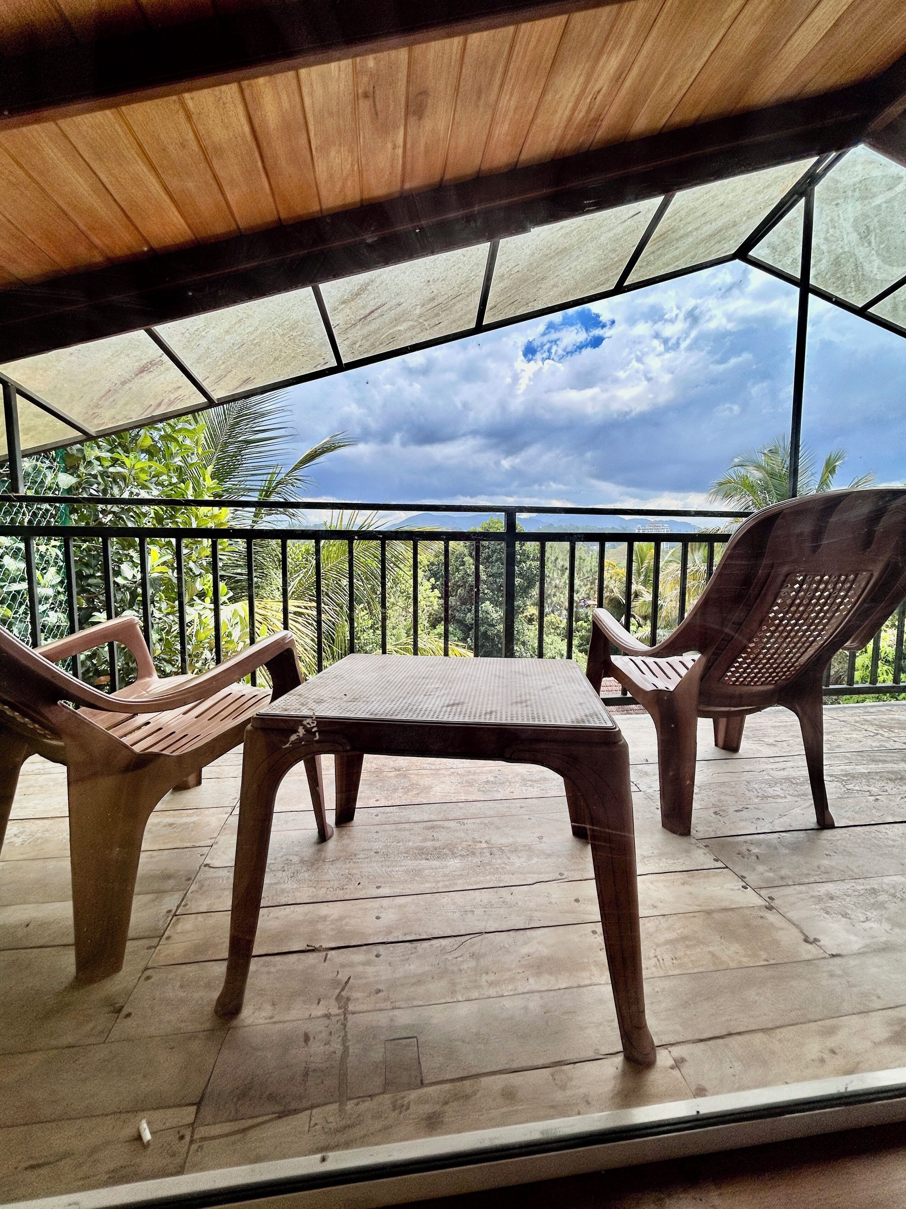 A covered outdoor seating area with a table and two chairs, overlooking a lush landscape.