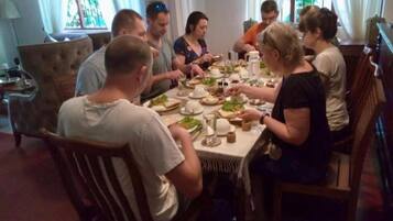 Un grupo de personas sentadas alrededor de una mesa de comedor en una habitación con una araña y una ventana con cortinas.