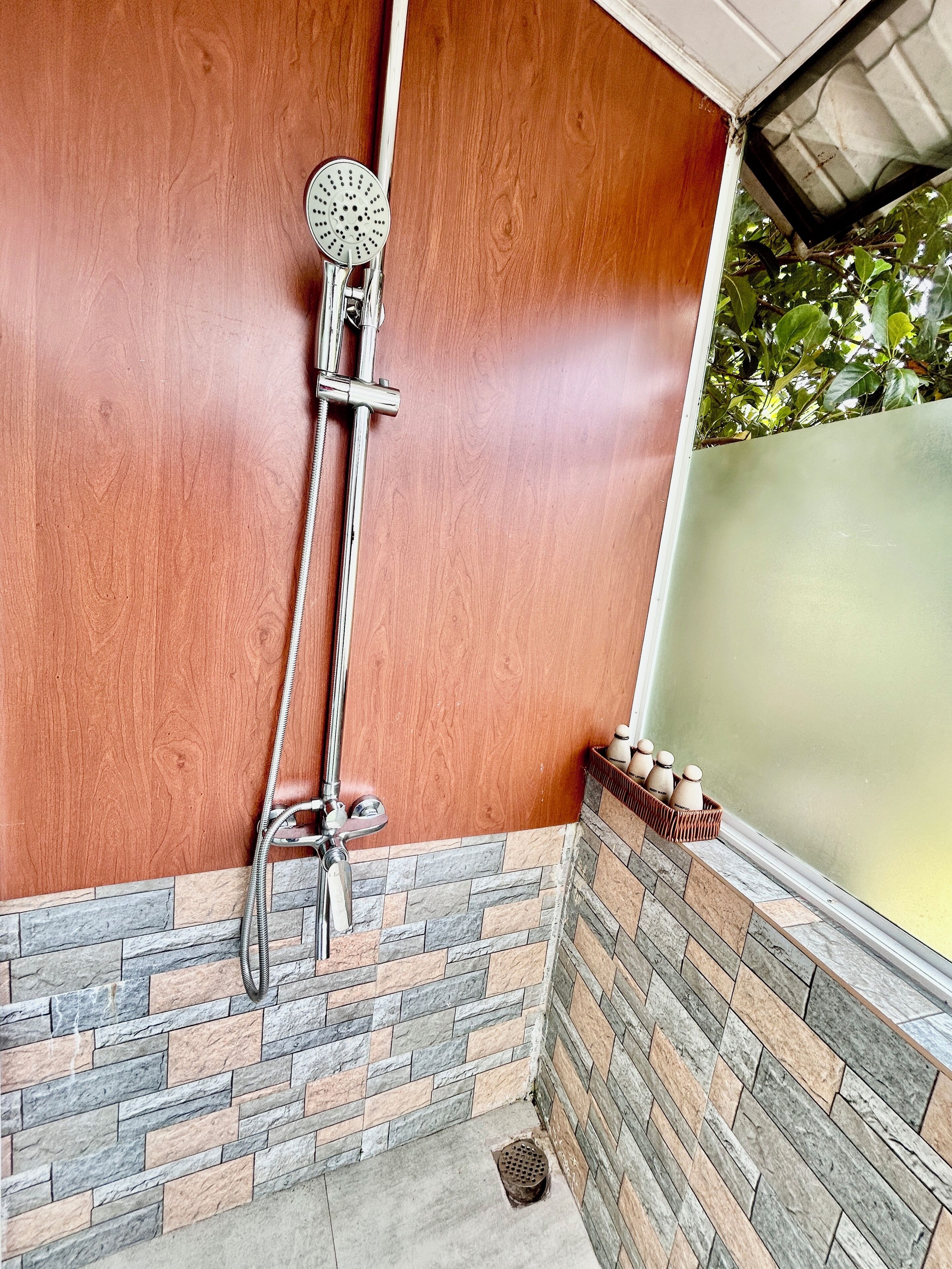 Un espacio de ducha con ducha de lluvia, pared de madera y suelo de baldosas de piedra.