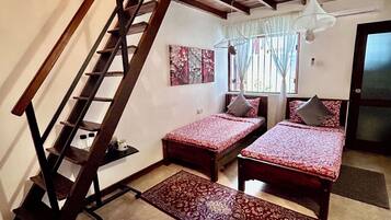 Ein Schlafzimmer mit einer Holztreppe, zwei Betten mit roter Bettwäsche, einem Fenster mit Vorhängen und einer hängenden Deckenleuchte.