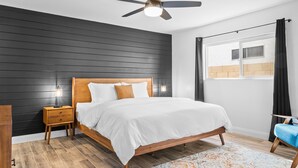 A bedroom with a wooden bed, a nightstand, a ceiling fan, and a window with curtains.