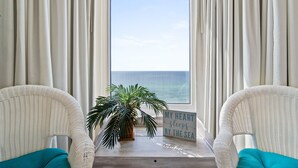 A room with two white wicker chairs, a small table with a sign, and a potted plant.