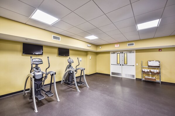 A fitness room with treadmills, a television, and a wall-mounted shelf with baskets.
