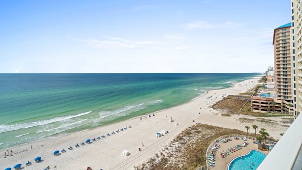 A beach view with a pool, beach umbrellas, and a tall building.