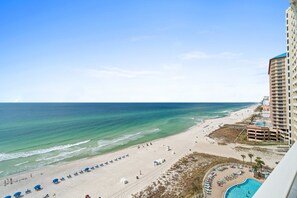 A beach view with a pool, beach umbrellas, and a tall building.