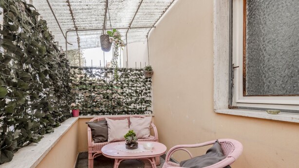 Un balcón con un sofá de mimbre rosa, una mesita redonda y plantas en macetas.
