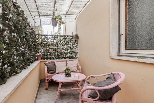 A balcony with a pink wicker sofa, a small round table, and potted plants.