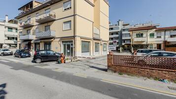 Un edificio residencial de varios pisos con balcones, entrada protegida por portón y coches estacionados.