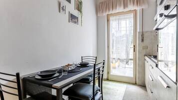 Comedor con una mesa lista para cuatro personas, sillas, ventana con vistas y zona de cocina con armarios y electrodomésticos.