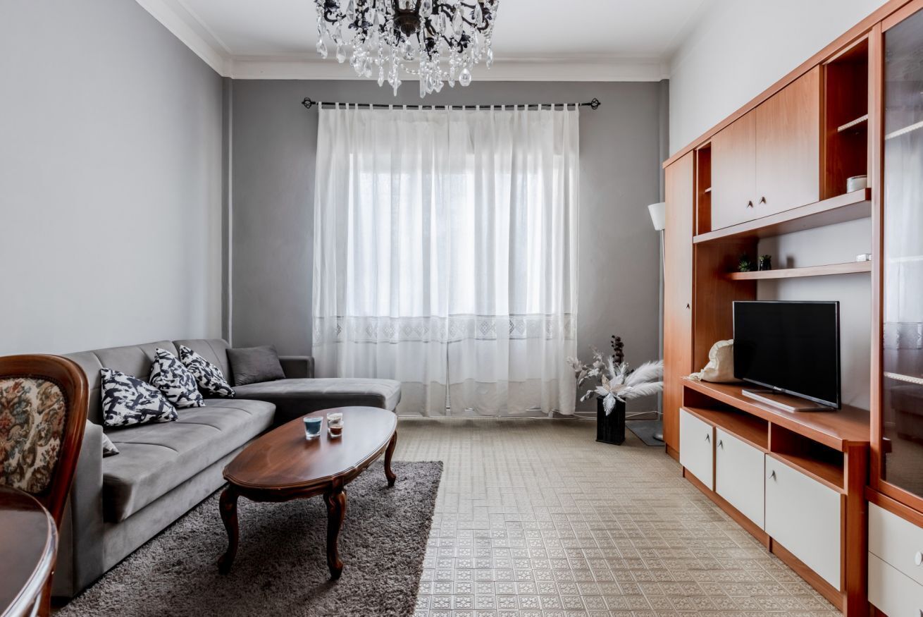 Un soggiorno con un divano grigio, un tavolino in legno, una TV su un mobiletto in legno e un lampadario.