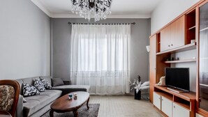Una sala de estar con un sofá gris, una mesa de centro de madera, un televisor sobre un mueble de madera y una araña.