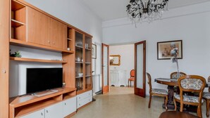 Una sala de estar con televisor, armarios de madera, una mesa de comedor con sillas y una araña.