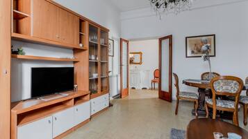 A living room with a TV, wooden cabinets, a dining table with chairs, and a chandelier.