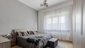 Un dormitorio con cama, mesita de noche, banco y cortinas.