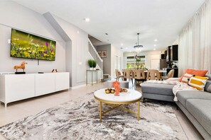 A modern living room with a white console, a round coffee table, a grey sofa, and a dining area in the background.