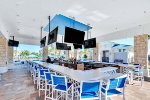 An outdoor bar area with multiple screens, seating, and a pool view.