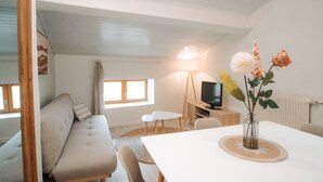 Un salon avec un canapé, une table à manger, un téléviseur et un vase rempli de fleurs.