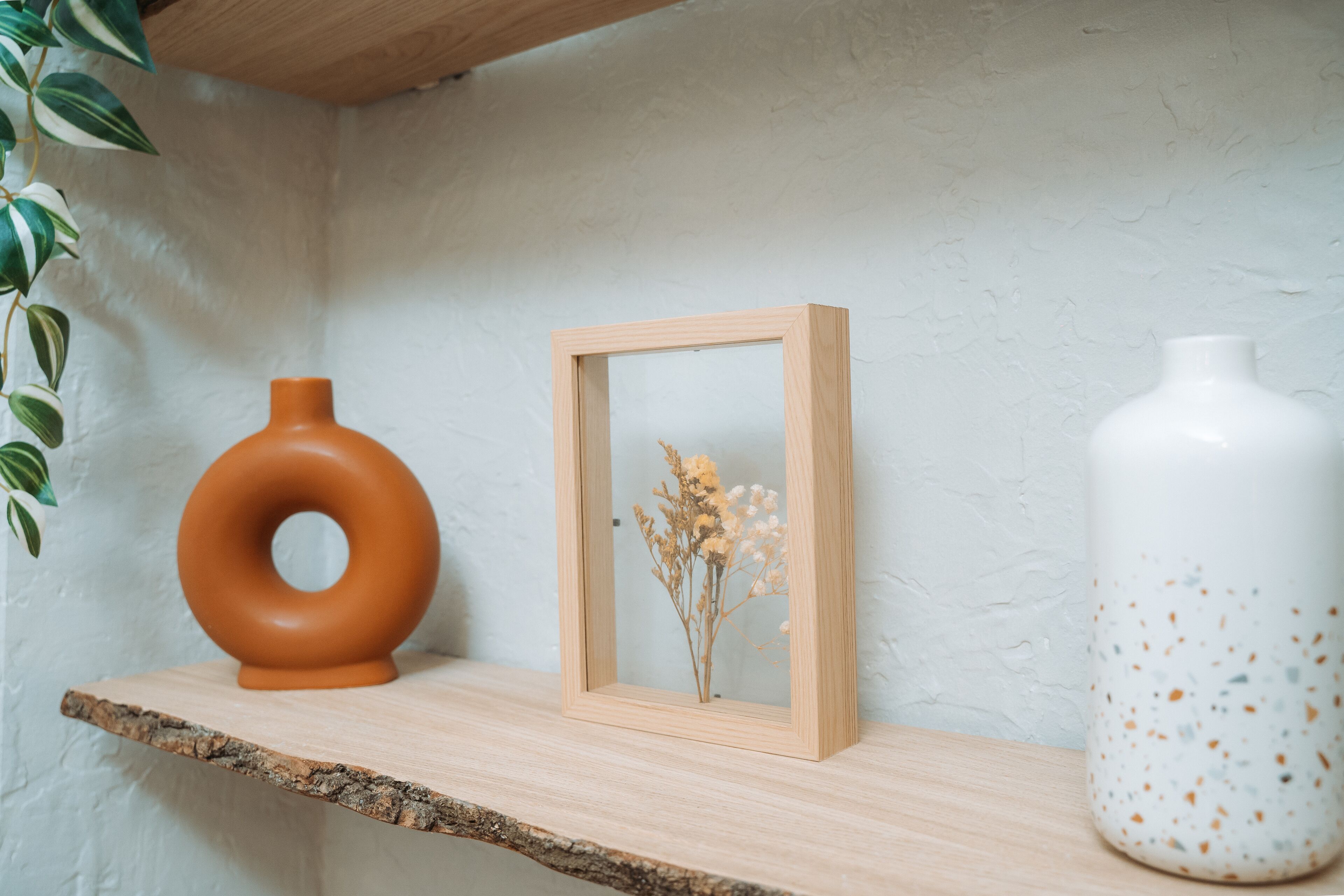 Ein Regal mit Holzrahmen, eine braune Vase und eine weiße Vase mit Tupfen.