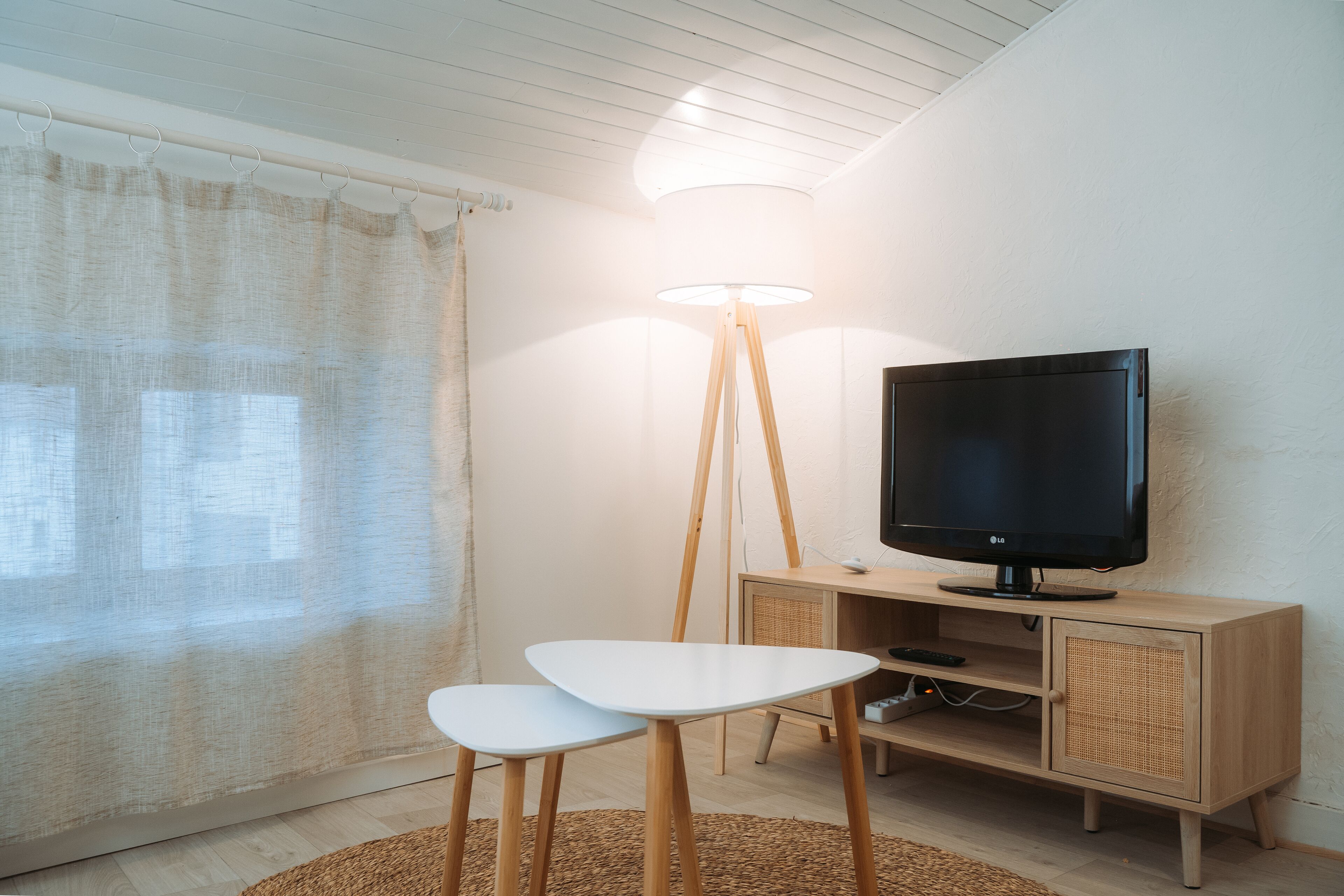 A modern living room with a television on a wooden cabinet, a floor lamp, and two white chairs.