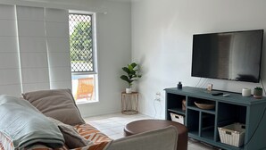A living room with a sofa, a television, and a ceiling fan. - Beach, Sand Relax (Bucasia)