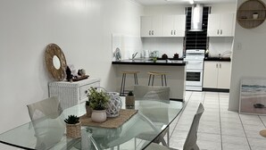 A modern kitchen with white cabinets, a glass dining table, and a stainless steel range hood. - Beach, Sand Relax (Bucasia)