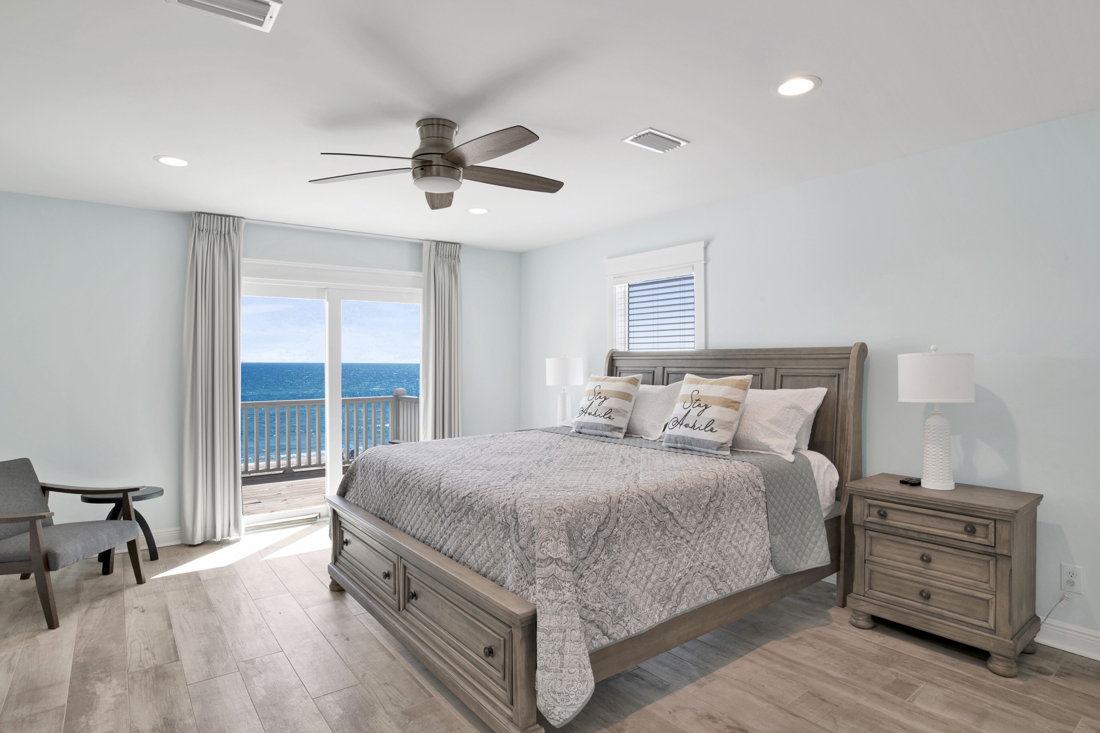A bedroom with a large bed, a nightstand, a chair, and a view of the ocean.