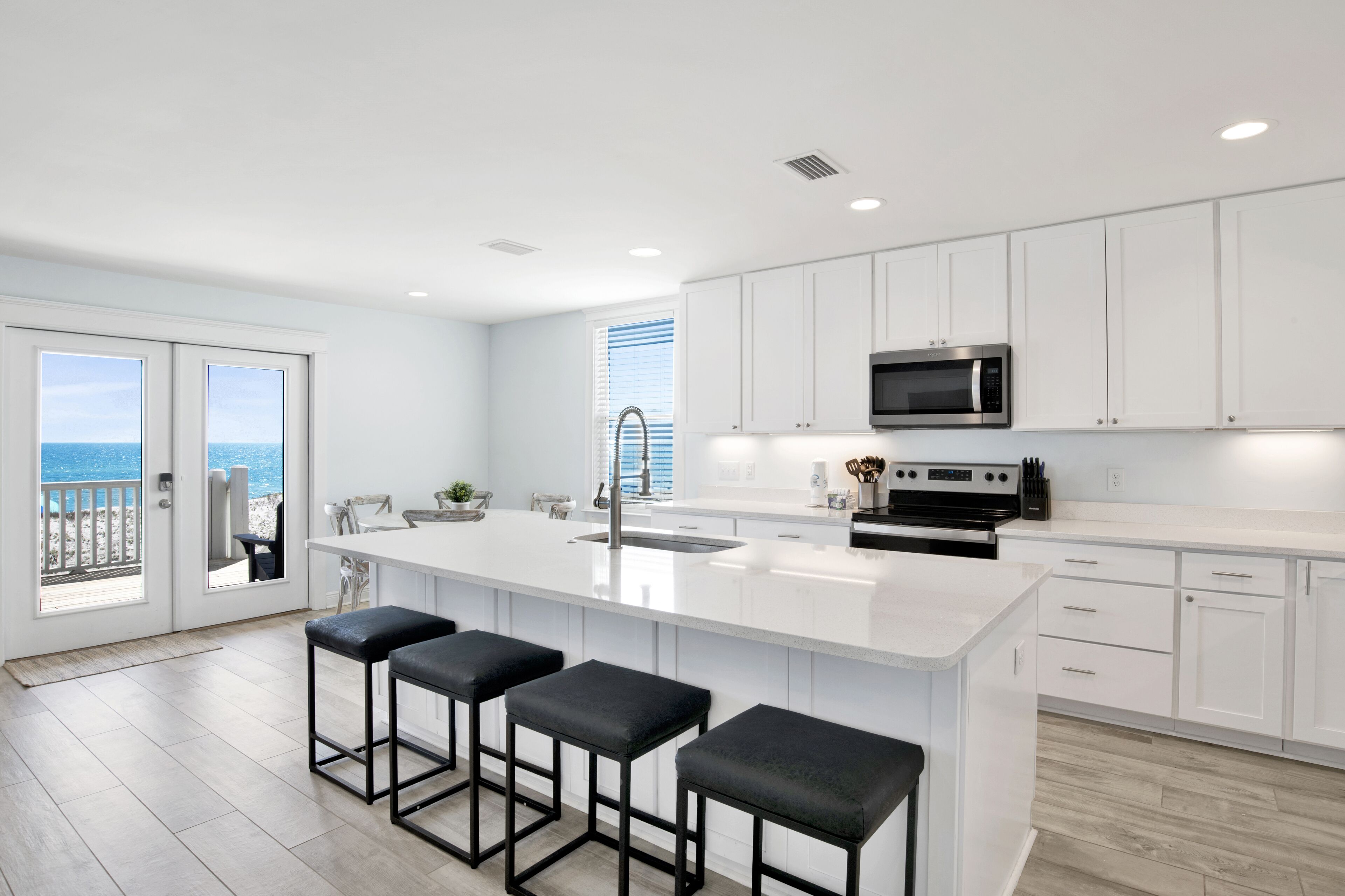 Una cocina moderna con armarios blancos, una isla grande con taburetes de bar, un microondas de acero inoxidable y vistas al exterior.