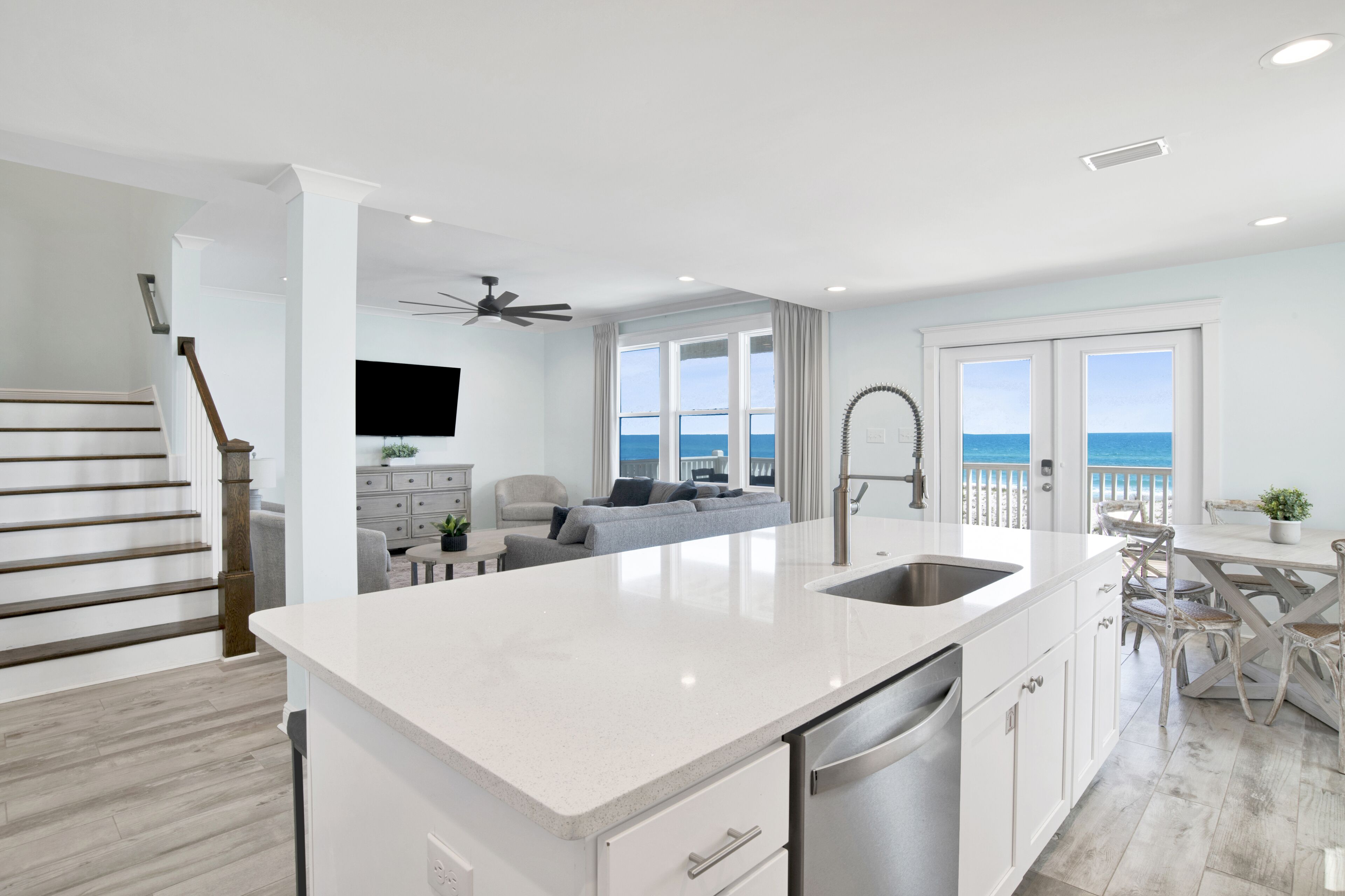 A modern kitchen with a large island, a dining area with a view, and a staircase leading to a balcony.