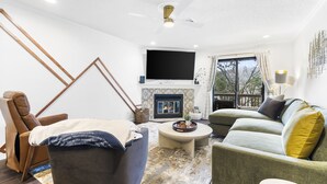 Ein modernes Wohnzimmer mit Kamin, Deckenventilator und großem Fernseher.