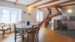 Un comedor con sillas de madera, una mesa con mantel estampado, un florero y una escalera que sube a otro nivel.