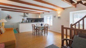 Amplia sala de estar con techo de madera, una mesa de comedor con sillas, un sofá y una cocina al fondo.