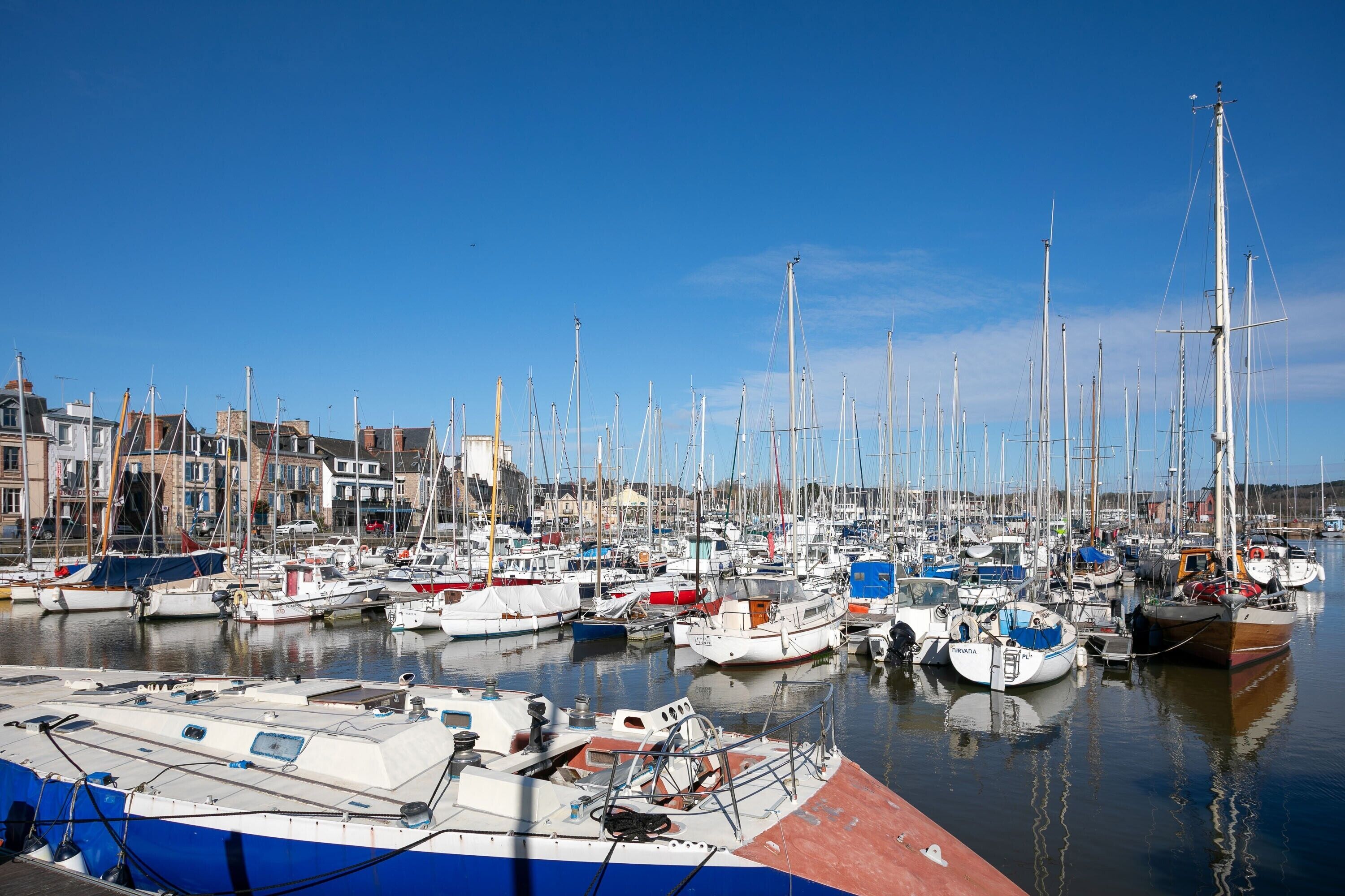 Un port de plaisance où de nombreux bateaux sont amarrés, des bâtiments qui bordent la rive et une eau calme.