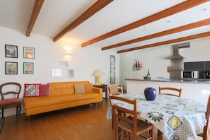 Un comedor con mesa dispuesta para cuatro, sillas de madera, un sofá y una cocina al fondo.