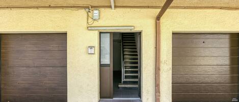 Um edifício com duas portas de garagem fechadas, um lance de escadas que levam à entrada e uma caixa de utilidades na parede.