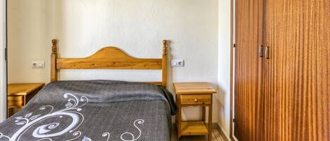 Une chambre avec un lit en bois, une table de chevet, une armoire et une prise électrique au mur.
