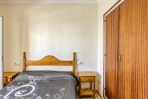 A bedroom with a wooden bed, a bedside table, a wardrobe, and a wall socket.