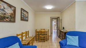 Una sala de estar con un sofá azul, una mesa de comedor de madera con sillas, y un pasillo que conduce a otra habitación.