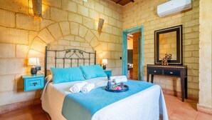 Camera con pareti in pietra, un letto, lampade da comodino, una cassettiera e uno specchio.