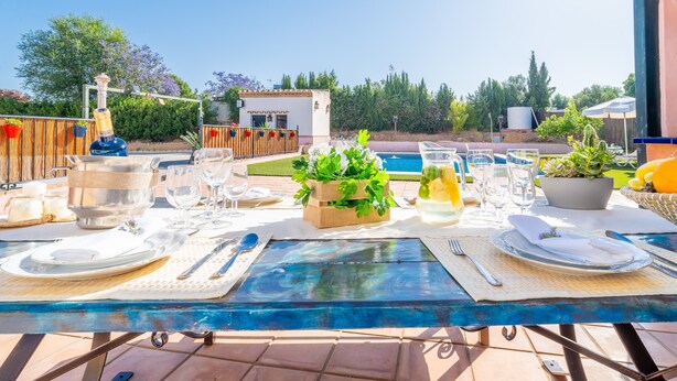 Area pranzo all'aperto con tavolo apparecchiato per due, una pianta in vaso e vista sulla piscina e sul verde.